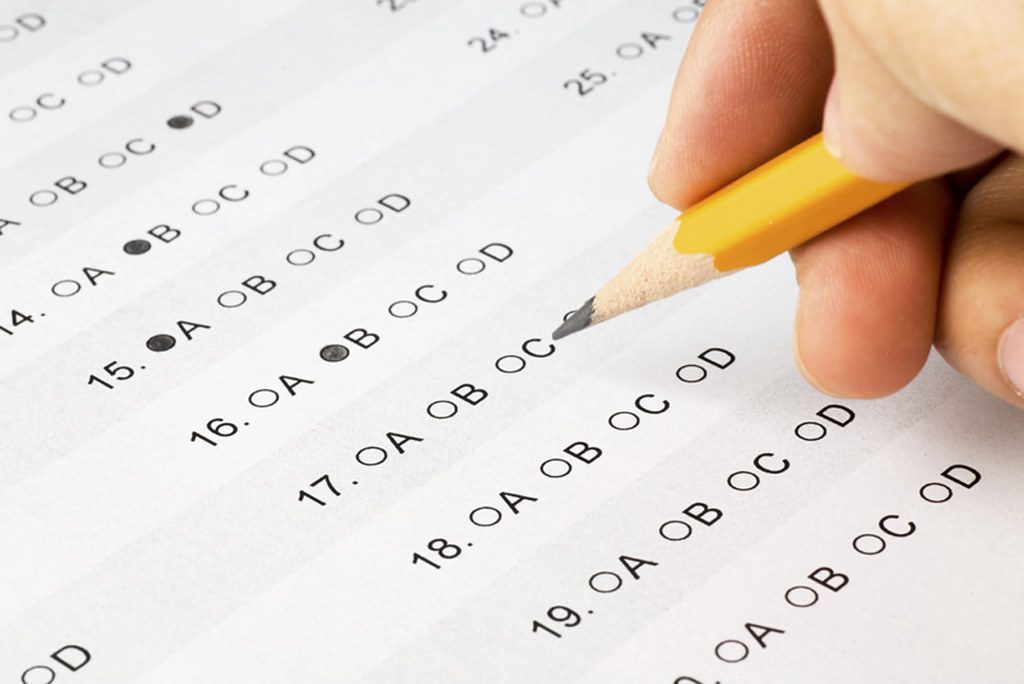 Main d'un candidat remplissant une copie d'examen au crayon