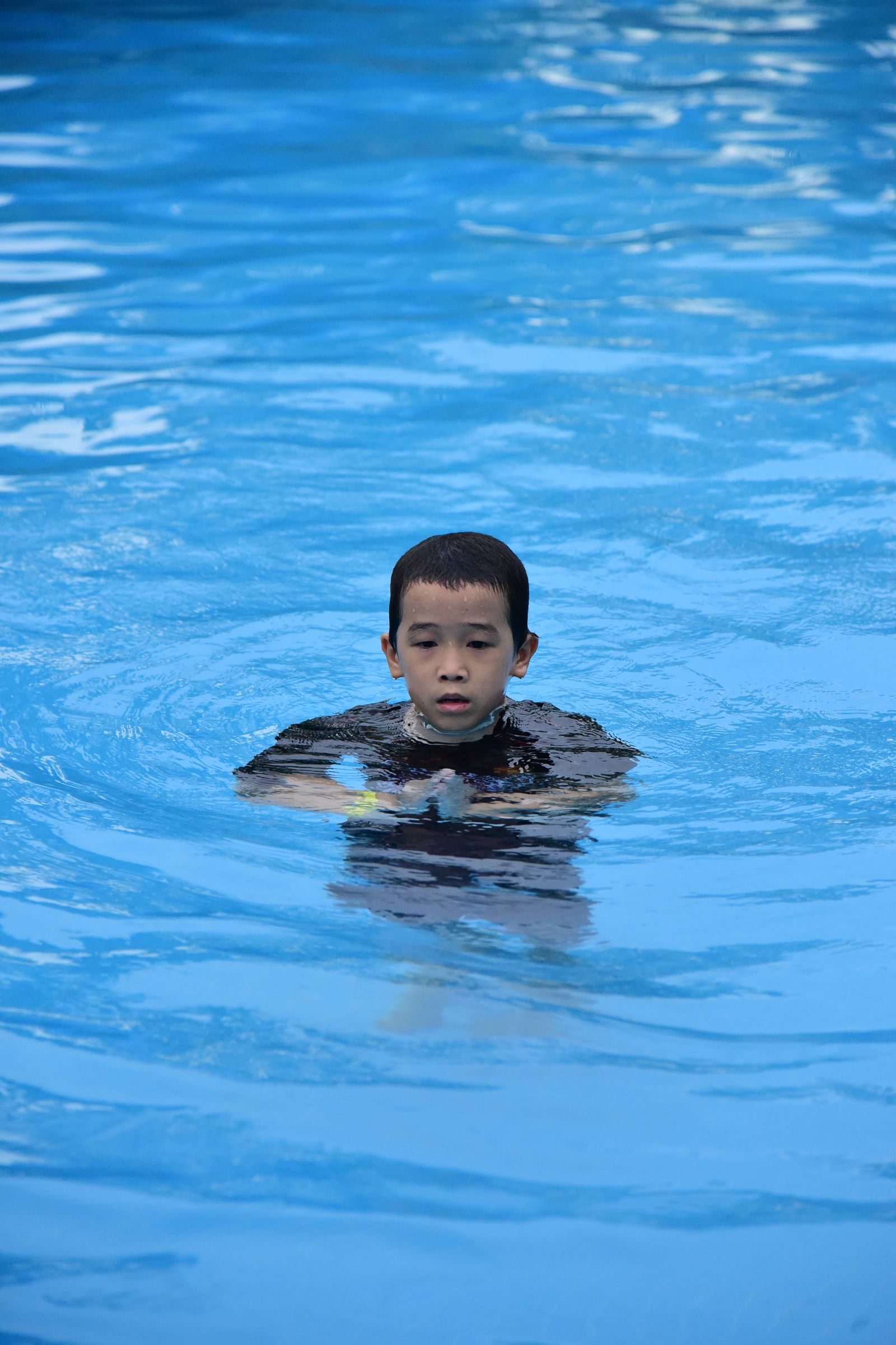 Un enfant nage dans une piscine exterieure sous la surveillance des adultes