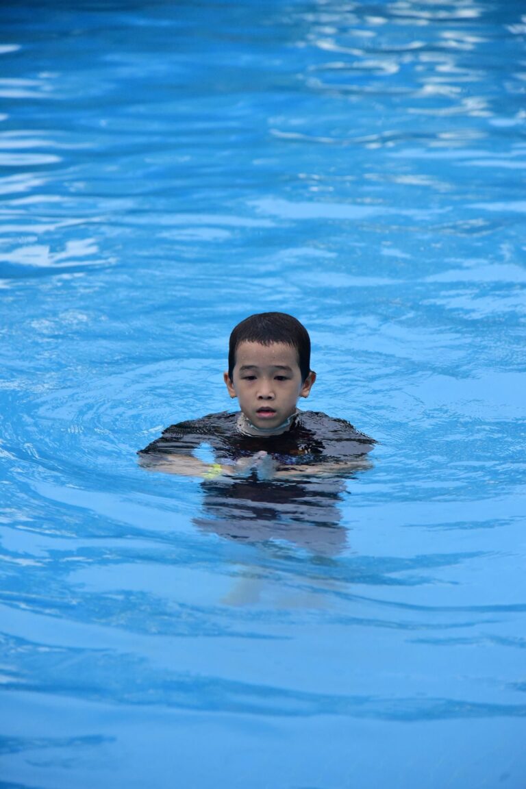 Un enfant nage dans une piscine exterieure sous la surveillance des adultes