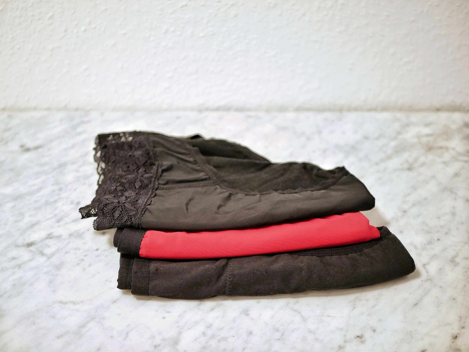 Trois culottes menstruelles pliées, posées sur un plan en marbre.