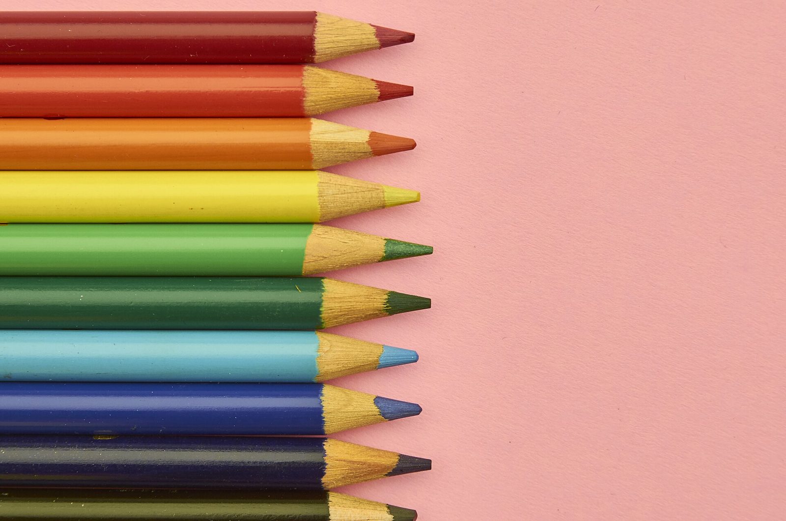 Crayons de couleur alignés sur une surface rose, illustrant les fournitures de la rentrée scolaire.