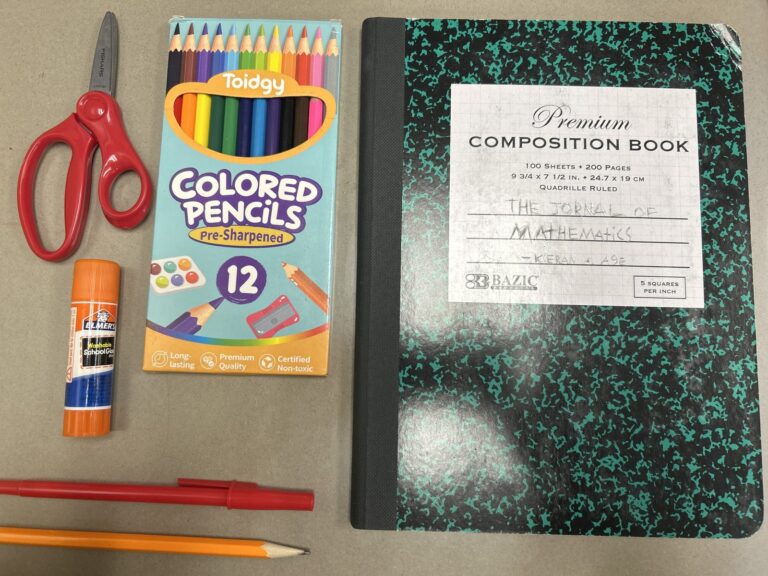 Fournitures scolaires posées sur une table : une paire de ciseaux, une boîte de crayons de couleur, un bâton de colle, deux stylos, un crayon à papier et un cahier à petits carreaux intitulé cahier de mathématiques.