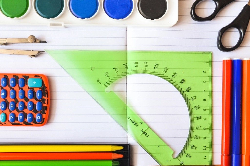 Fournitures scolaires : peinture, ciseaux, compas, calculatrice, équerre et crayons de couleur posés sur un cahier