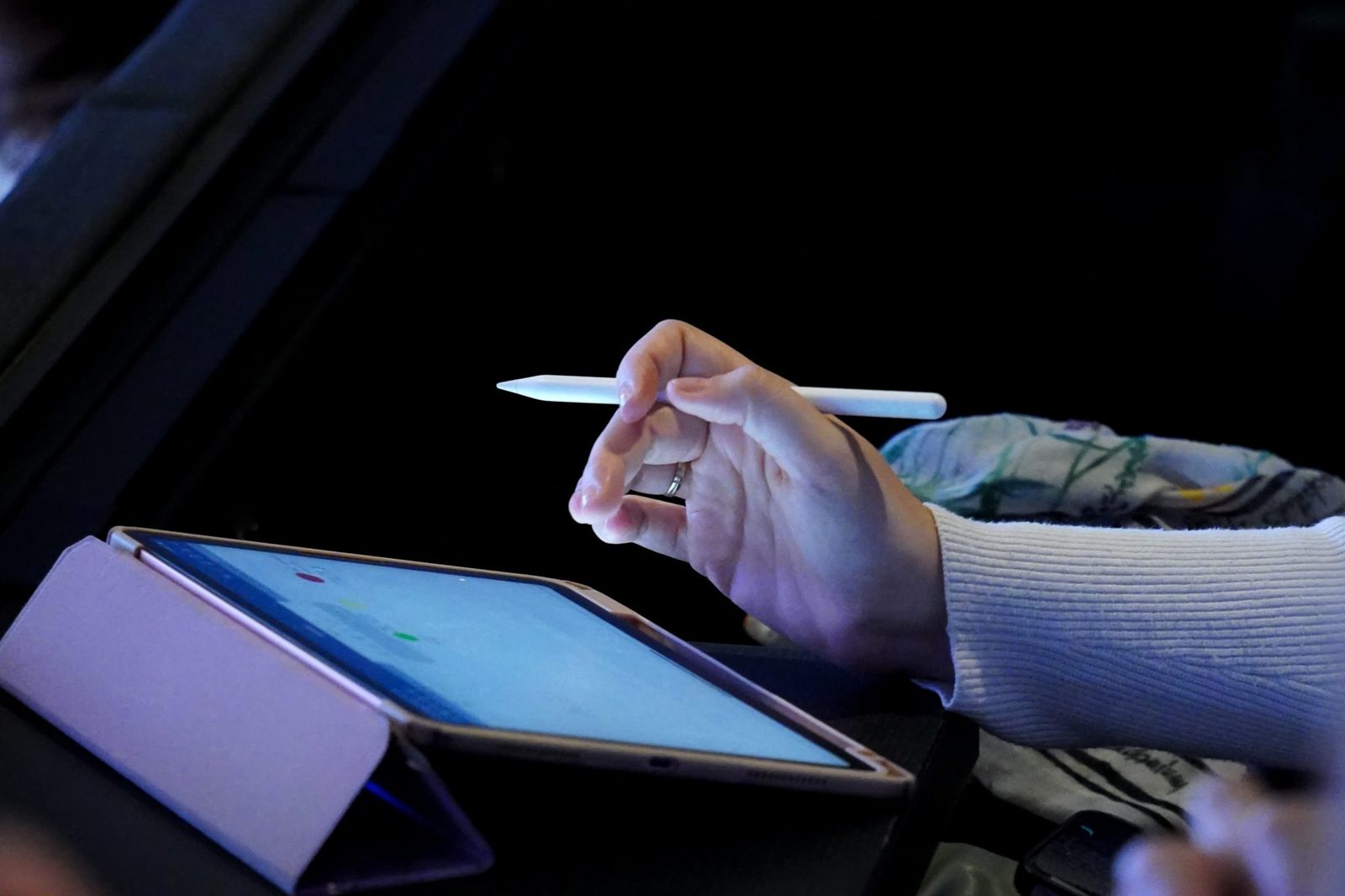 Une main utilise un stylet sur l'écran d'une tablette tactile.
