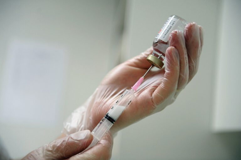 Des mains gantées prélèvent une dose dans un flacon à l'aide d'une seringue.