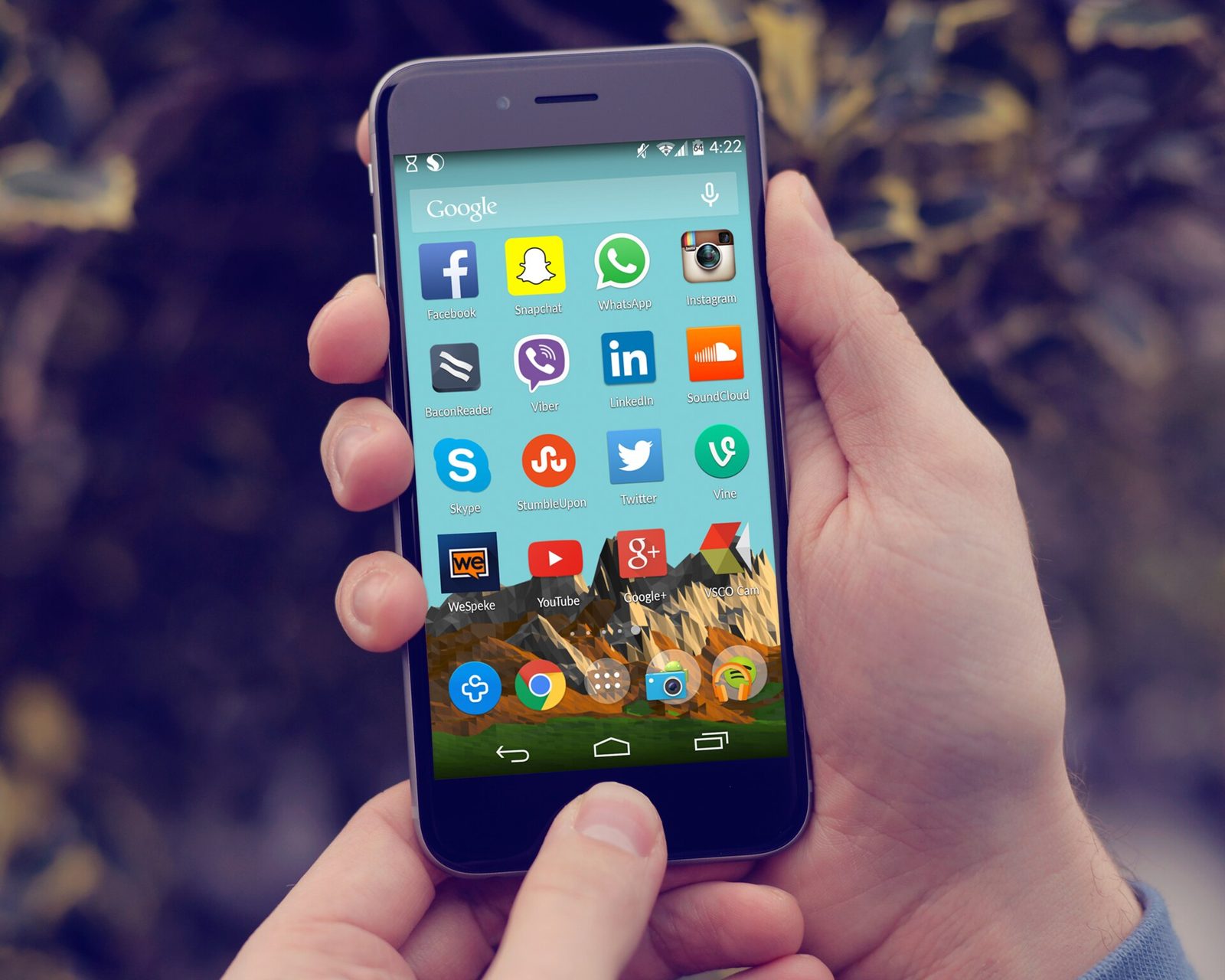 Une main tient un smartphone dont l'écran affiche de nombreuses applications de réseaux sociaux.