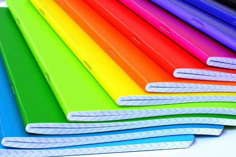 Une pile de cahiers d'écolier aux couvertures colorées, pages lignées visibles sur la tranche.