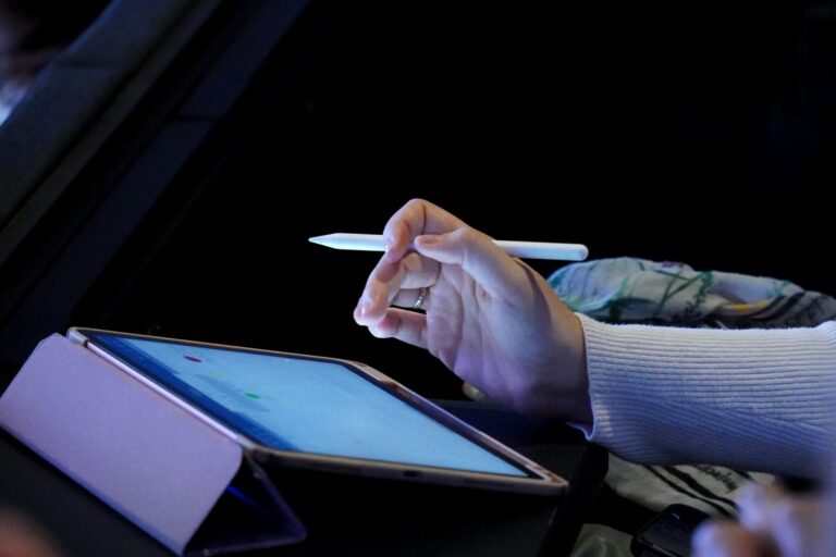 Une main utilise un stylet sur l'écran d'une tablette tactile.