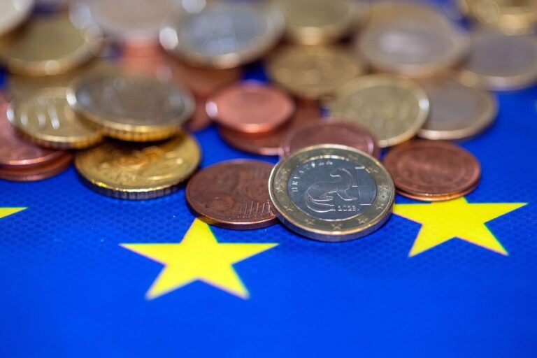 Pièces en euros posées sur un drapeau européen, illustrant le paiement d'un impôt.