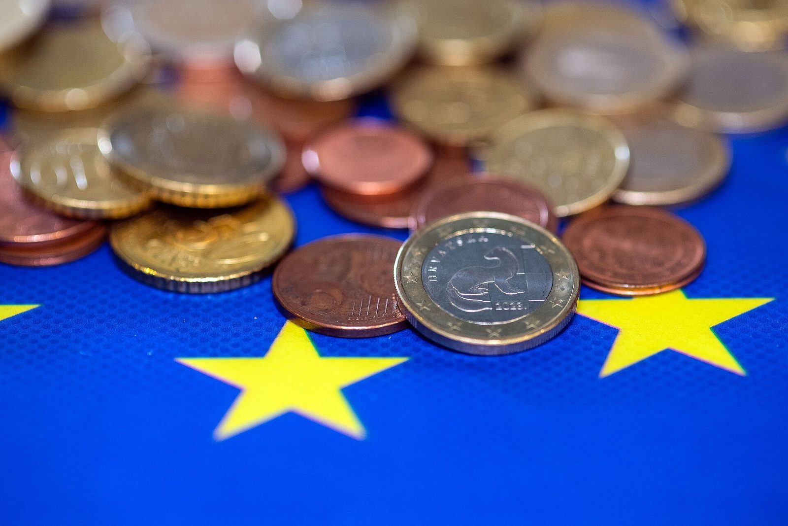 Pièces en euros posées sur un drapeau européen, illustrant le paiement d'un impôt.
