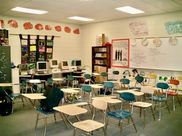 Salle de classe de lycée vide, avec des tables-chaises, un tableau blanc et des affiches réalisées par les élèves