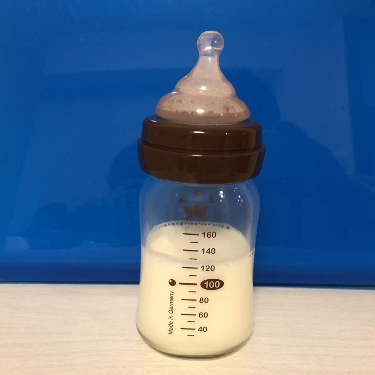 Biberon en verre gradue rempli de lait, pose devant un fond bleu.